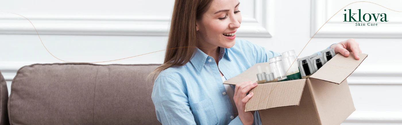 Mujer sonriente abriendo un paquete de productos Iklova Skin Care recibiendo su rutina completa de cuidado facial.